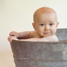 a baby sitting in a metal tub with his head turned to the side and smiling