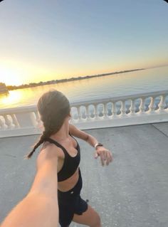 a woman is running on the sidewalk by the water with her arm extended to the camera