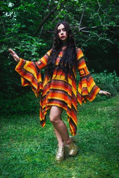 a woman in an orange and yellow crocheted dress is walking through the grass