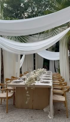 an outdoor wedding setup with white draping and flowers on the table, surrounded by wooden chairs