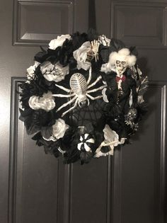 a wreath decorated with black and white flowers, skeleton decorations and spider web hanging from the front door