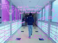 a man walking down a long hallway covered in pink and white writing on the walls