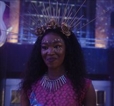 a woman in a pink dress with flowers on her head and makeup is smiling at the camera