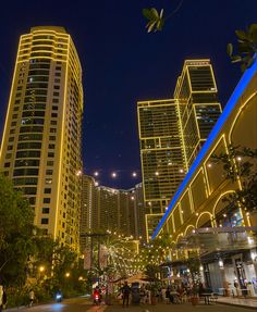 the city is lit up at night and people are walking down the street in front of tall buildings