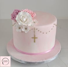 a pink cake decorated with flowers and a cross on the top is sitting on a table