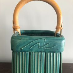 a green ceramic basket with bamboo handles on a table