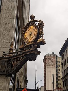 a large clock mounted to the side of a building on a city street next to tall buildings