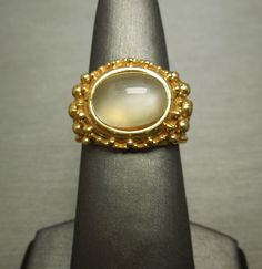 "Vintage Circa 1970 in an Ancient Roman Style Constructed of Sterling Silver Accented with a Gold Plating Containing 1 Genuine Earth-Mined Oval Natural Moonstone weighing approximately 4.70 carats Moonstone measuring approximately 11.5mm in length x 8.3mm in width Top section of ring measuring approximately 15.1mm (0.60\") in length Inside shank: 925 Finger Size 7.25 *Sizing upon request (Sizing down runs about $25.. Sizing up starts at $45) Weighing 10.7 grams *Sale of ring includes an appraisa Gold Moonstone Ring Collectible, Gold Cabochon Moonstone Ring Collectible, Collectible Gold Hallmarked Moonstone Ring, Vintage Gold Moonstone Ring For Anniversary, Vintage Oval Moonstone Ring With Polished Finish, Vintage Gold Moonstone Anniversary Ring, Vintage Cabochon Moonstone Ring For Anniversary, Vintage Yellow Gold Moonstone Ring, Vintage Round Cabochon Moonstone Ring