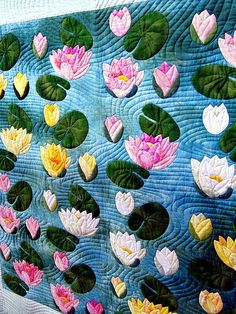 a quilted wall hanging with water lilies on it's sides and green leaves in the middle