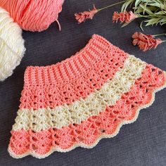 a crocheted pink and white skirt next to some yarn on a gray surface