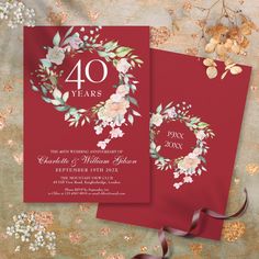 two red wedding cards with floral wreaths and ribbons on them, sitting next to each other