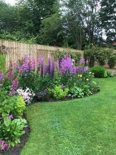 a garden filled with lots of flowers next to a wooden fence and green grass covered ground