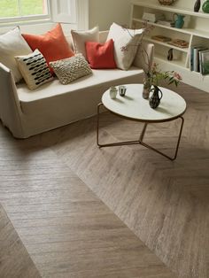 a living room with wood flooring and white couches, coffee table and bookshelf