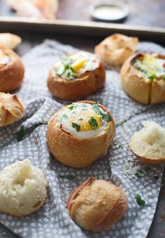 baked breads with eggs in them on a cloth covered tablecloth, ready to be eaten