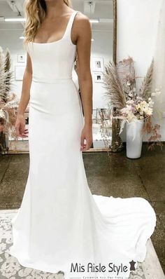 a woman standing in front of a mirror wearing a white wedding dress with spaghetti straps