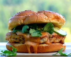 a chicken sandwich with cheese and lettuce on a wooden cutting board next to a window