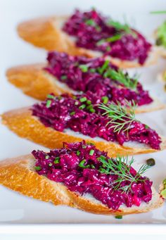 several pieces of bread topped with red cabbage and garnish on a white plate