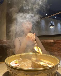 a woman sitting in front of a bowl of soup with chopsticks sticking out of it