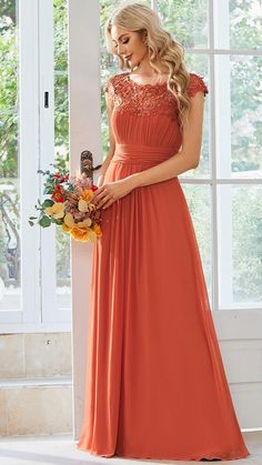 a woman standing in front of a window wearing an orange dress and holding a bouquet