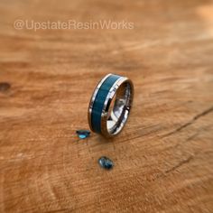 a wedding band with blue and white inlays sits on top of a wooden table