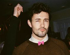 a man with a pink bow tie standing in front of a person wearing a brown sweater