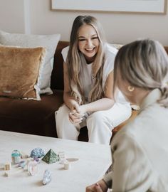 two women sitting at a table playing with wooden blocks and dices on the floor