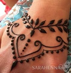 a woman's hand is decorated with black henna and leaves on the wrist