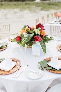 the table is set with white linens, gold chargers and tropical floral centerpieces