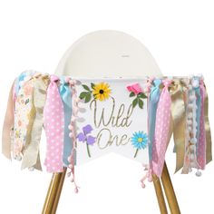 a white sign with pink, blue and yellow flowers on it that says wild one