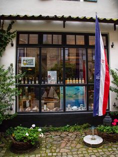 an outside view of a store with flowers in the foreground and a flag on display