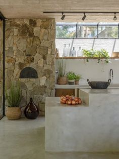 an outdoor kitchen with stone walls and flooring is shown in this image, there are potted plants on the counter next to the sink