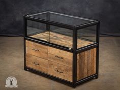 a wooden and glass display case with drawers on wheels in front of a black wall