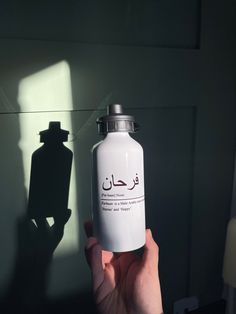 a person holding up a white bottle in front of a wall with a shadow on it