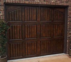 a brown garage door in front of a brick building with potted plants on the side