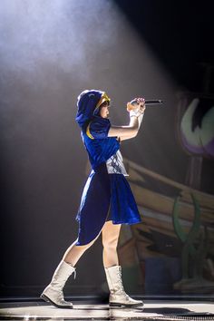 a woman in a blue dress and white boots holding a microphone while standing on stage