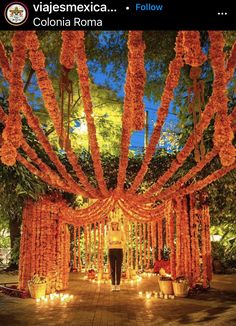 a man standing in front of an orange flower covered archway with candles on the ground