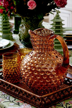 a glass pitcher sitting on top of a wooden tray next to other glasses and plates