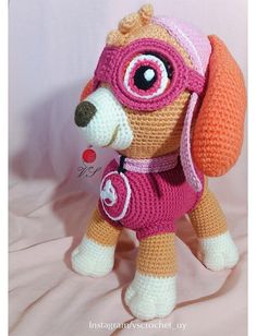 a crocheted stuffed dog with goggles and a pink hat on it's head