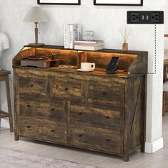 a wooden dresser with drawers in a living room next to a lamp and pictures on the wall