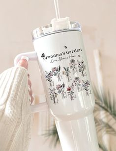 a woman holding a white coffee cup with flowers on it and the words grandma's garden printed on it