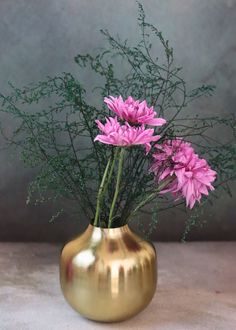 some pink flowers are in a gold vase