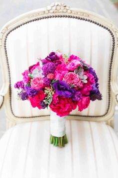 a bridal bouquet sitting on top of a white chair with purple and pink flowers