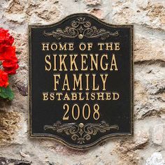 a plaque on the side of a stone building with red flowers in front of it