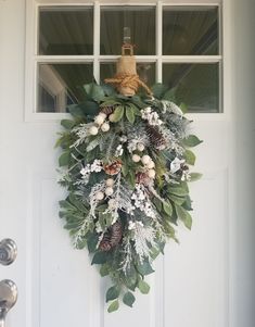 a wreath hanging on the front door of a house with pine cones and greenery