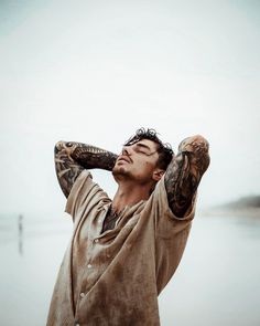 a man with tattoos on his arms and hands is standing by the water looking up