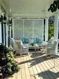 a covered porch with white wicker furniture and blue pillows on it's sides