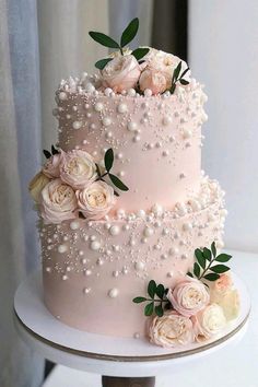 a three tiered wedding cake with white flowers and pearls on the top, sitting on a table