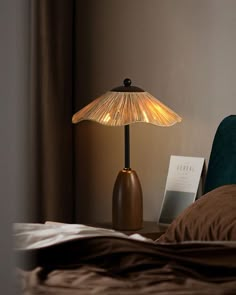 a lamp on a bedside table next to a bed with brown sheets and pillows in a bedroom