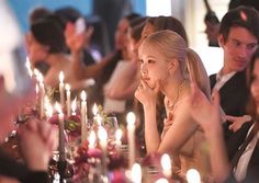 a group of people sitting at a table with candles in front of them and one woman looking up