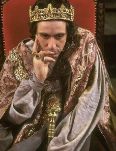 a man sitting in a chair wearing a crown and holding his hand to his face